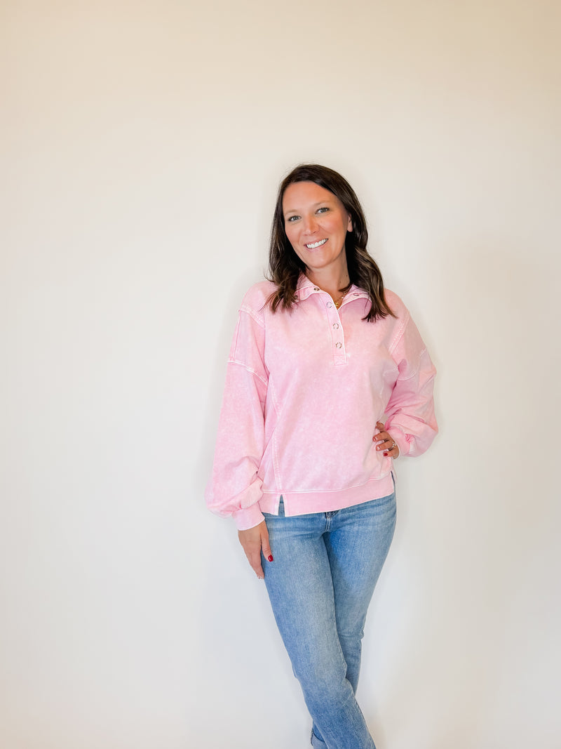 Women's pink Henley pullover sweatshirt with a vintage washed finish, balloon sleeves, and a relaxed fit. Features a button-up neckline and ribbed hem for a stylish and cozy look. Perfect for casual wear, layering, and effortless everyday fashion. Paired with classic blue jeans for a trendy, laid-back outfit.