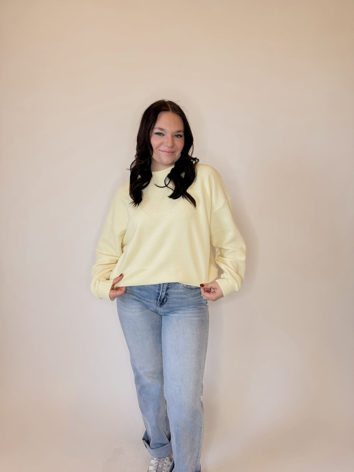 Women's pastel yellow waffle knit sweatshirt with a relaxed fit, long sleeves, and ribbed cuffs. Styled with light-wash straight-leg jeans and casual sneakers for a trendy and cozy everyday look. Perfect for layering in fall, winter, and spring fashion.