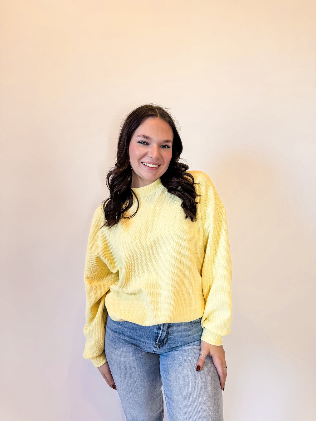 Women's pastel yellow waffle knit sweatshirt with a relaxed fit, long sleeves, and ribbed cuffs. Styled with light-wash straight-leg jeans and casual sneakers for a trendy and cozy everyday look. Perfect for layering in fall, winter, and spring fashion.