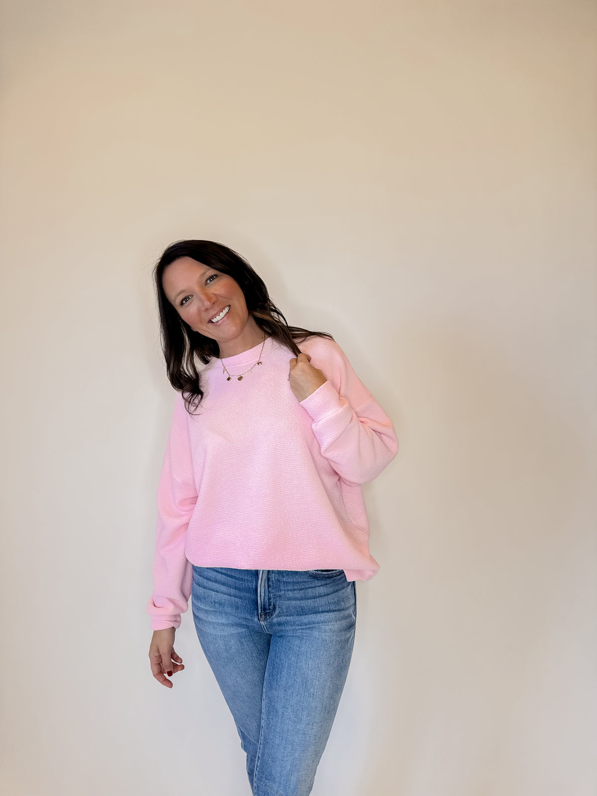 Women's pink crewneck sweatshirt with a textured knit design, long sleeves, and a relaxed fit. Styled with classic blue jeans for a casual and cozy everyday outfit. Perfect for layering in fall, winter, and spring fashion. Soft and comfortable pullover sweater for effortless style.