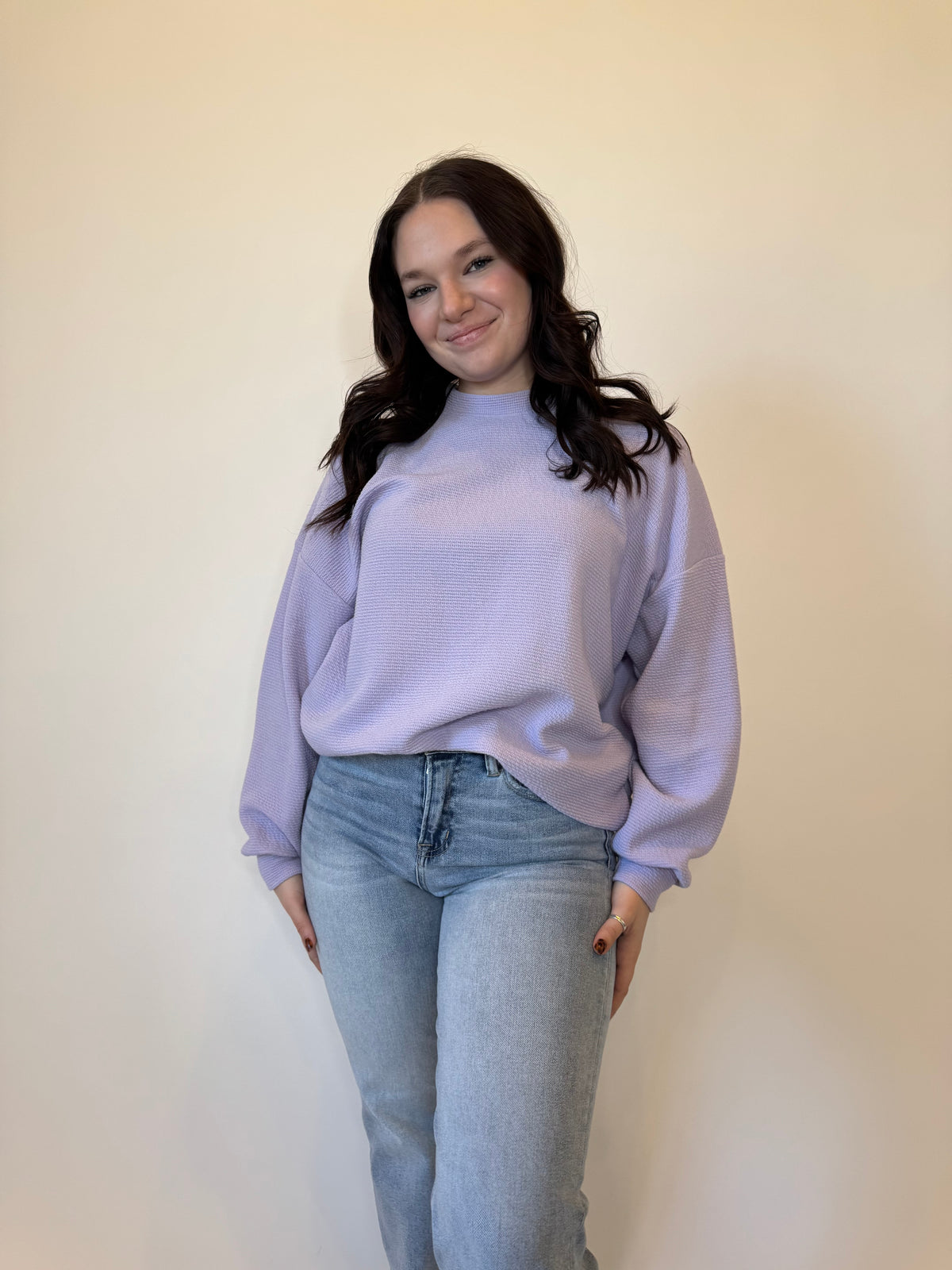 Women's lavender purple oversized sweatshirt with a textured waffle knit design, featuring a relaxed fit and long sleeves. Styled with light-wash straight-leg jeans and casual sneakers for a trendy, effortless look. Perfect for cozy everyday wear, layering, and casual fashion in fall, winter, and spring.