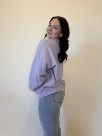 Women's lavender purple oversized sweatshirt with a textured waffle knit design, featuring a relaxed fit and long sleeves. Styled with light-wash straight-leg jeans and casual sneakers for a trendy, effortless look. Perfect for cozy everyday wear, layering, and casual fashion in fall, winter, and spring.